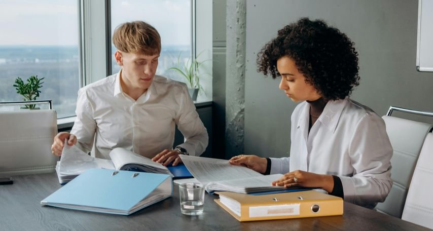 Colleagues in White Long Sleeve Shirts Sitting and Reading a report